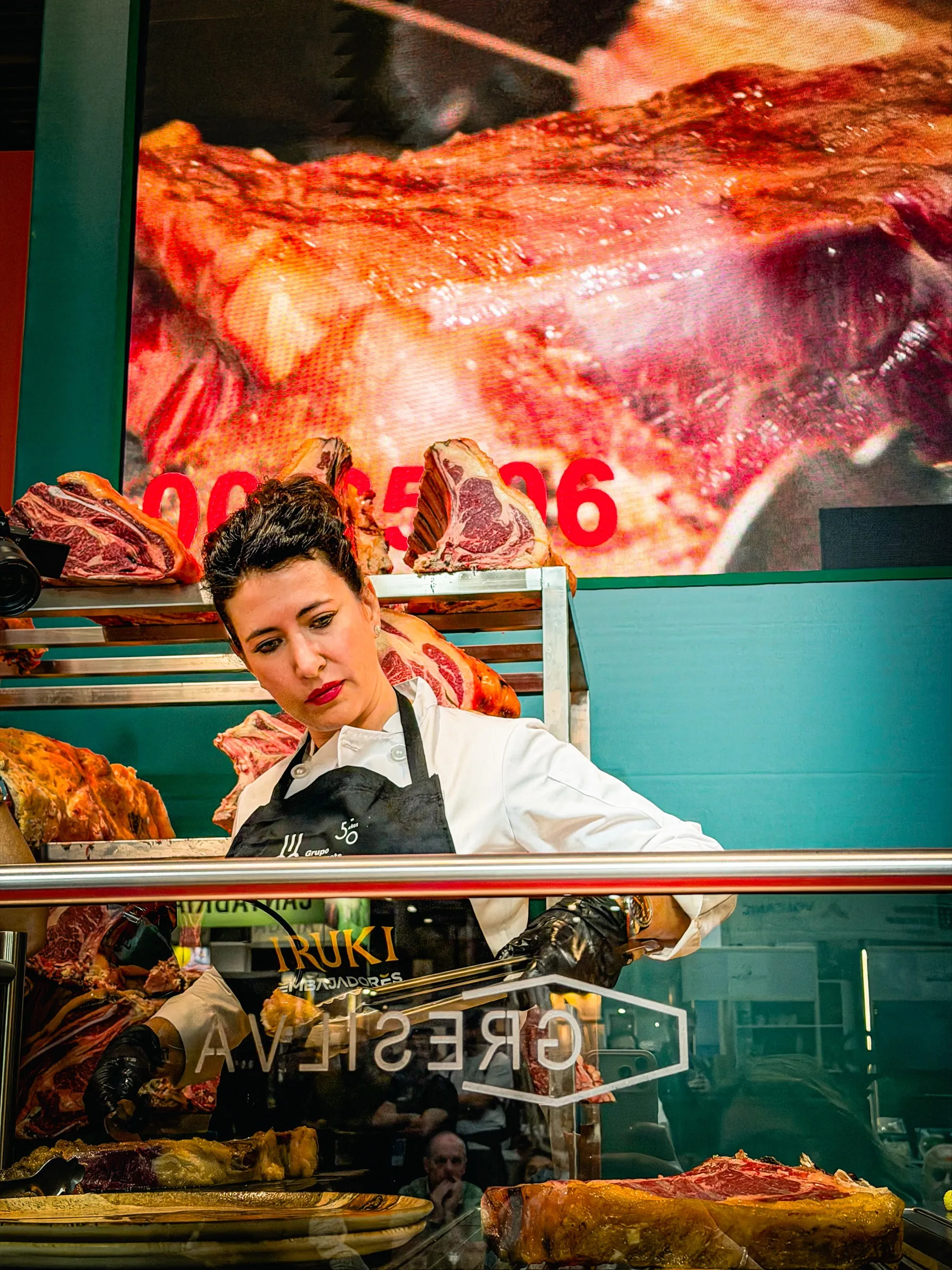 Davinia Martínez trincha carne a la brasa tras el mostrador, entre piezas de vacuno madurado