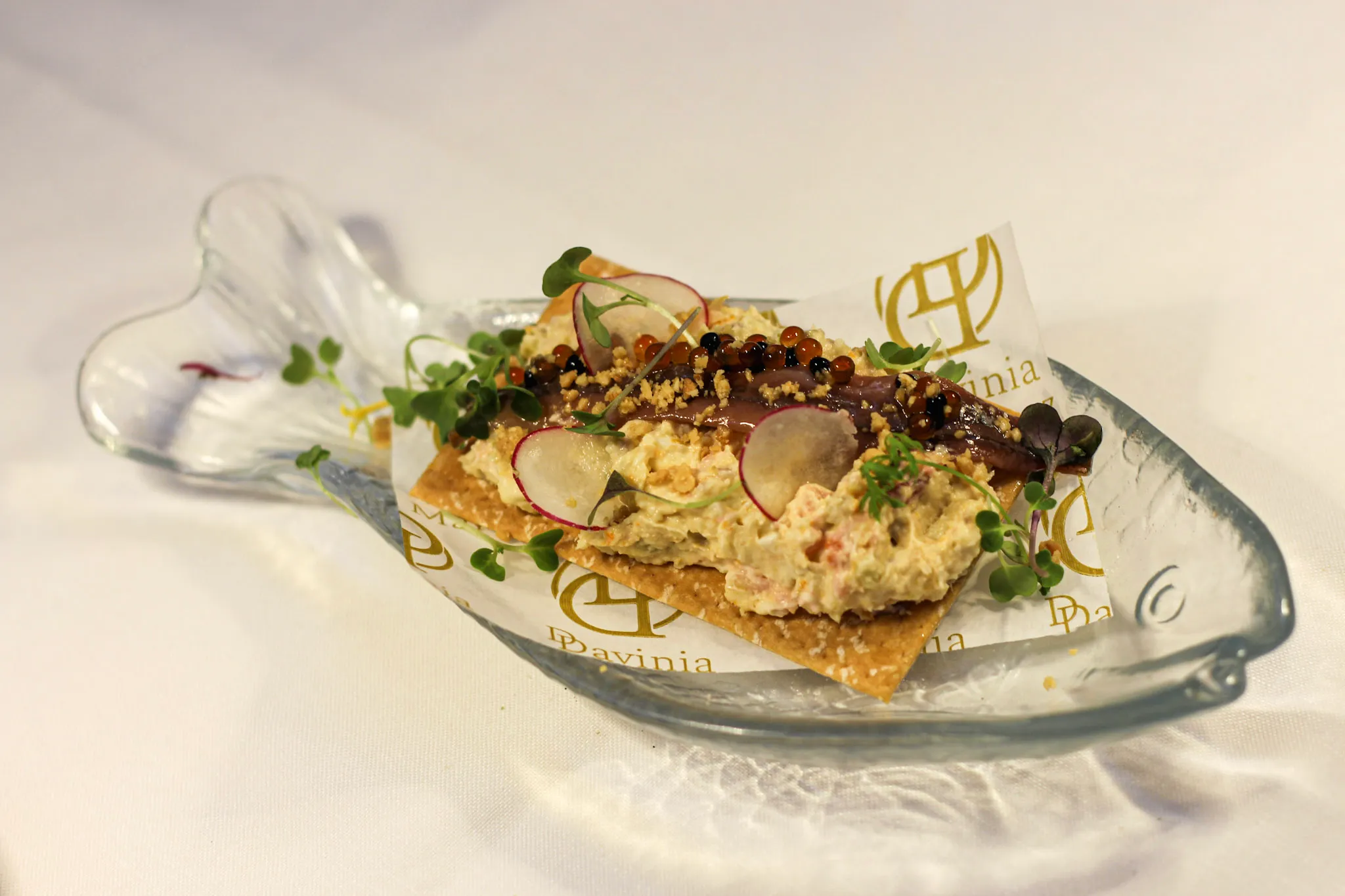 Aperitivo sobre cracker en plato de cristal con la marca Davinia
