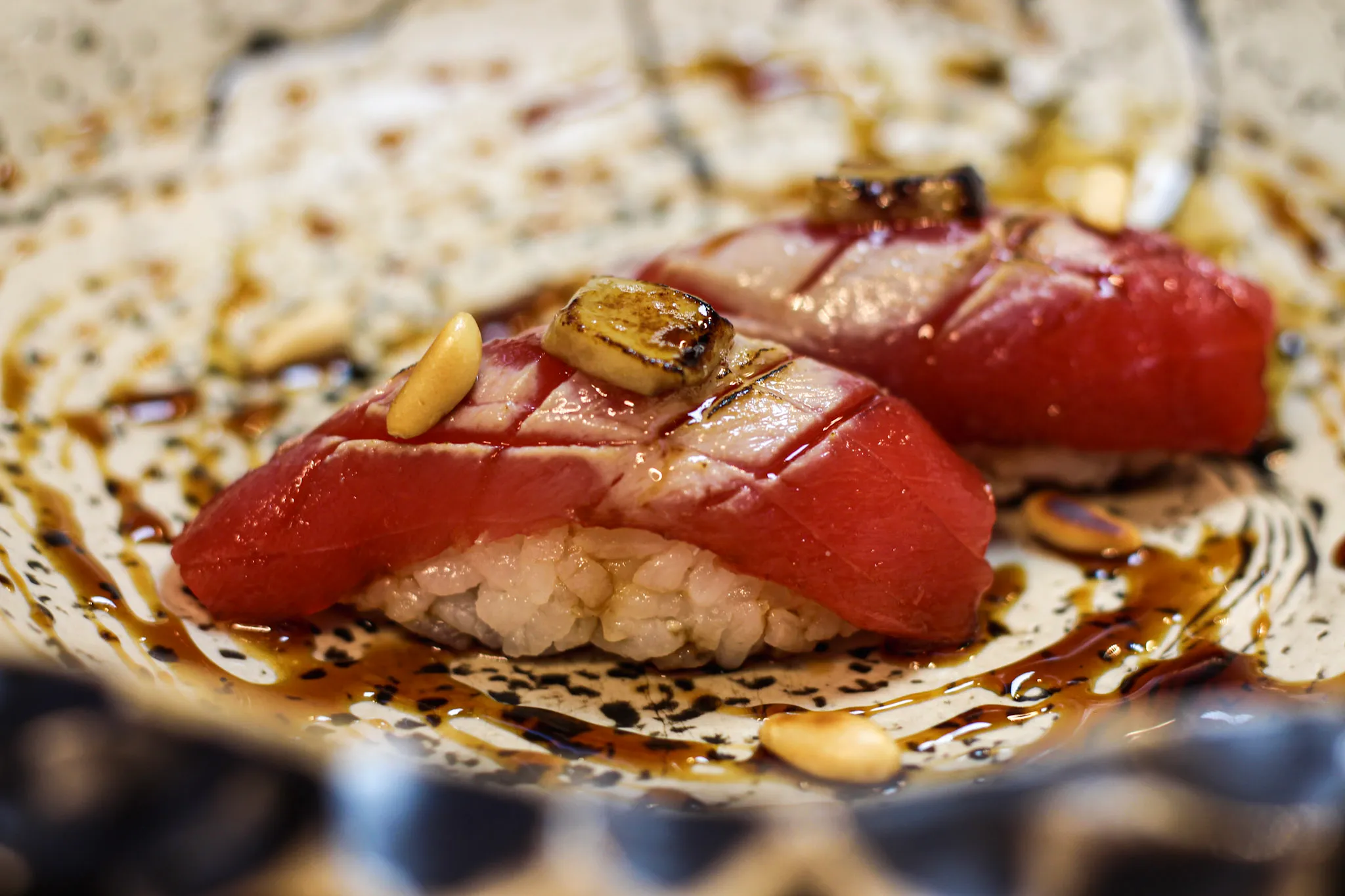 Nigiri de atún rojo con piñones sobre plato de cerámica oscura
